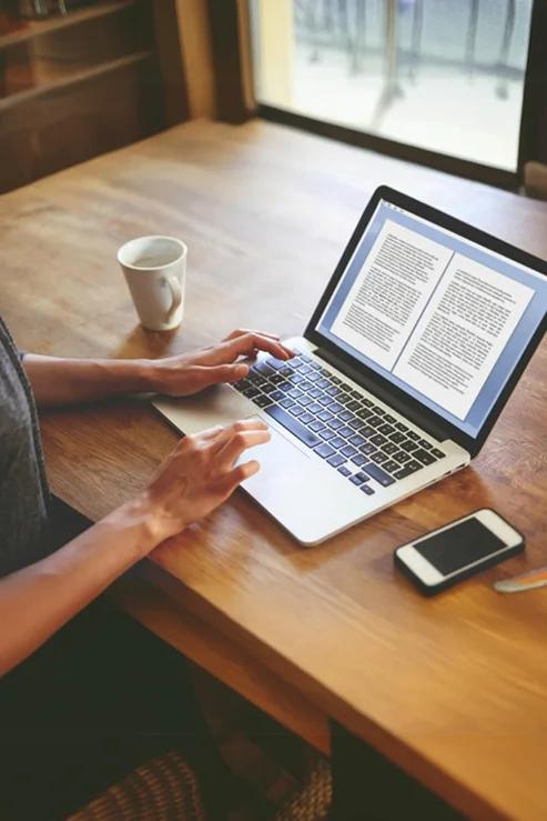 Author formatting a manuscript on a laptop at a wooden desk
