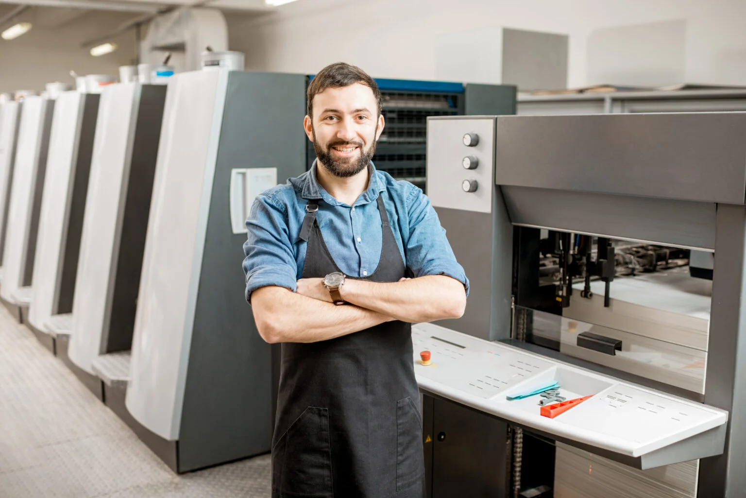 Print technician standing on the press floor next to commercial printing equipment